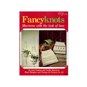 May include: A book cover with a red background and the title "Fancyknots: Macrame with the look of lace". The cover features two macrame projects: a plant hanger and a purse. The book is by Judy Peacher and Lucille Hammons and includes 14 projects.