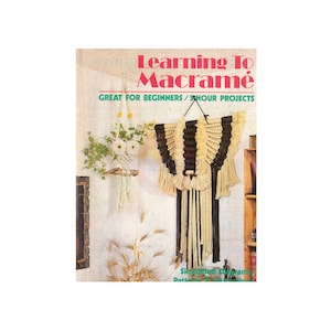 May include: Book cover with the title "Learning To Macrame" and the subtitle "Great for Beginners / 3-Hour Projects". The cover features a macrame wall hanging with black and white yarn.