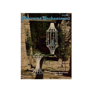 May include: A book titled "Macrame Enchantment" Book 5, featuring a white macrame lamp and table. The text "Norwegian Wood Lamp and Table" is printed below the image.