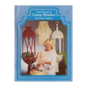 Könnte beinhalten: Buchcover mit dem Titel "Lamp Shades Macramé Lightly" von Snell Publications. Das Cover zeigt eine Frau und mehrere Makramee-Lampenschirme in verschiedenen Stilen und Farben, darunter ein Hängekorb und eine Tischlampe.