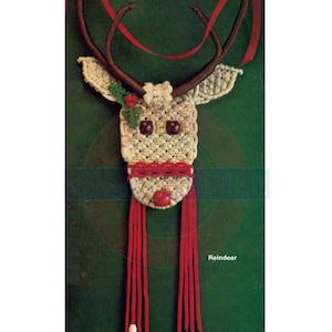 May include: A brown and white crocheted reindeer ornament with red yarn tassels and wooden beads. The reindeer has a red nose and brown antlers. The ornament is hanging from a red ribbon against a green background. The text "Reindeer" is printed below the ornament.