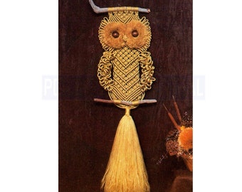 May include: A handmade macrame owl wall hanging. The owl features a golden-yellow color scheme with a fluffy head and a long tassel. The owl is made with knotted rope and is mounted on a wooden branch.