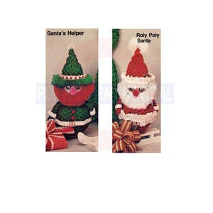 Op de afbeelding: Twee gehaakte kerstfiguren: "Santa's Helper" en "Roly Poly Santa". De Santa's Helper heeft een groene hoed en outfit met een rood gezicht. De Roly Poly Santa heeft een rode hoed en witte baard. Beide hebben strikken.