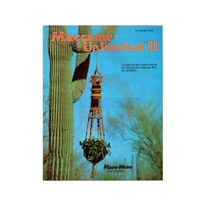 Puede incluir: Una portada de libro vintage para "Macramé Unlimited II" con un colgador de plantas de macramé colorido colgado de un cactus saguaro. La portada del libro es azul con texto blanco y muestra un colgador de plantas de macramé que contiene una planta verde.