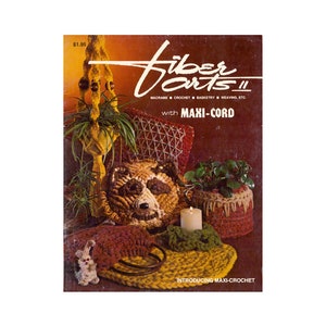 May include: A vintage book cover titled "Fiber Arts II" featuring macrame, crochet, basketry, and weaving projects. The cover showcases various handmade items, including a bear-shaped pillow, a plant holder, and a candle holder. The book is introducing Maxi-Crochet.