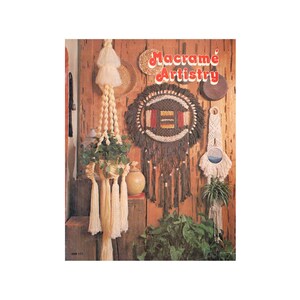 May include: A book cover featuring the title "Macrame Artistry" in red and white letters. The cover shows a variety of macrame wall hangings and plant hangers in different colors and patterns.