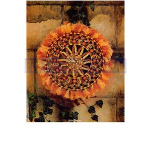 May include: A macrame wall hanging with a circular design featuring a sunburst pattern. The macrame is made with brown and orange cord and has a fringe border. The centre of the sunburst has a circle of brown beads.