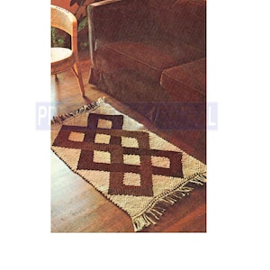 Op de afbeelding: Een geweven bruin en crèmekleurig tapijt met een geometrisch patroon van vierkanten. Het tapijt heeft franjes aan de randen en ligt voor een bruine bank.