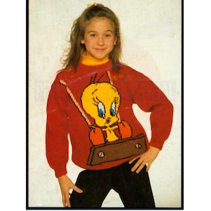 Op de afbeelding: Een rode gebreide trui met een gele Tweety Bird-afbeelding. Tweety houdt een bruine koffer vast en zit op een schommel. De trui heeft een gele rolkraag.