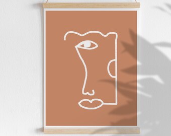 May include: Abstract art print featuring a minimalist line drawing of a face. The artwork is rendered in white against a terracotta background. The print is displayed with a wooden frame and a hanging string, creating a modern aesthetic.
