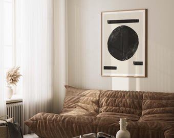 May include: A framed abstract art print featuring a large black circle and horizontal black bars on a cream background. The artwork hangs above a brown velvet sofa in a well-lit room. The room also includes a coffee table and a vase.