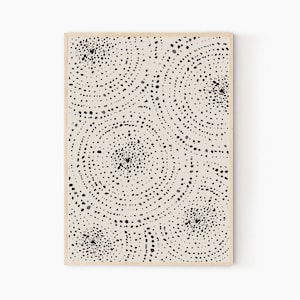 May include: A framed print featuring an abstract design in black and white. The design consists of a series of concentric circles with black dots on a beige background.