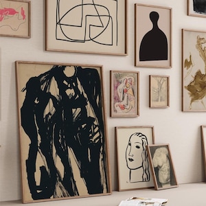 May include: A gallery wall with various framed art prints. The prints feature abstract designs, black and white line drawings, and a silhouette of a person. The prints are arranged in a grid pattern on a white wall.