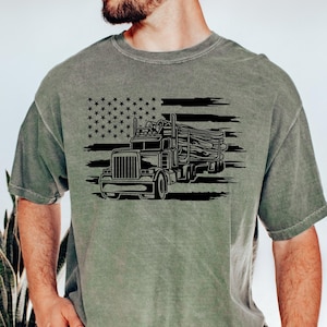 May include: A green t-shirt with a black and white graphic of a semi-truck hauling logs in front of an American flag.