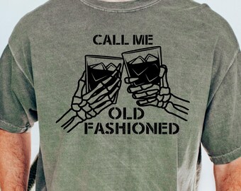 May include: A green t-shirt with a black graphic of two skeleton hands holding up glasses of whiskey. The text "Call me old fashioned" is printed below the glasses.
