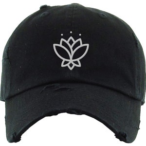 May include: A black distressed baseball cap with a white embroidered lotus flower design.