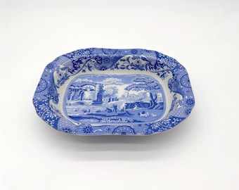 May include: A blue and white ceramic serving dish with a landscape scene in the center. The dish has a scalloped edge and floral patterns. The landscape scene depicts a bridge, trees, and figures.