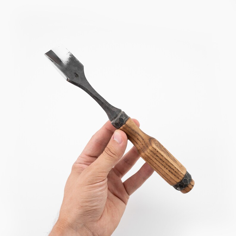 May include: A wood carving chisel with a black metal blade and a wooden handle with a dark brown stain. The handle has a metal band with decorative rivets.