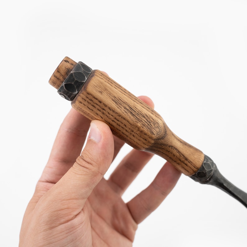 May include: A close-up of a wooden handled chisel with a metal head. The handle is made of dark wood with a grain pattern. The metal head is black and has a textured surface.