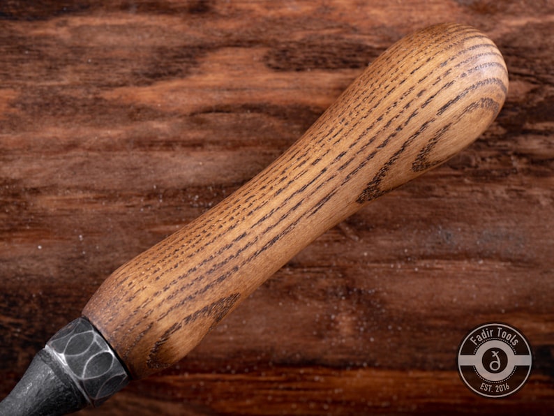 May include: Close-up of a wooden handle with a dark brown stain. The handle is smooth and has a slight curve. The handle is attached to a metal tool.