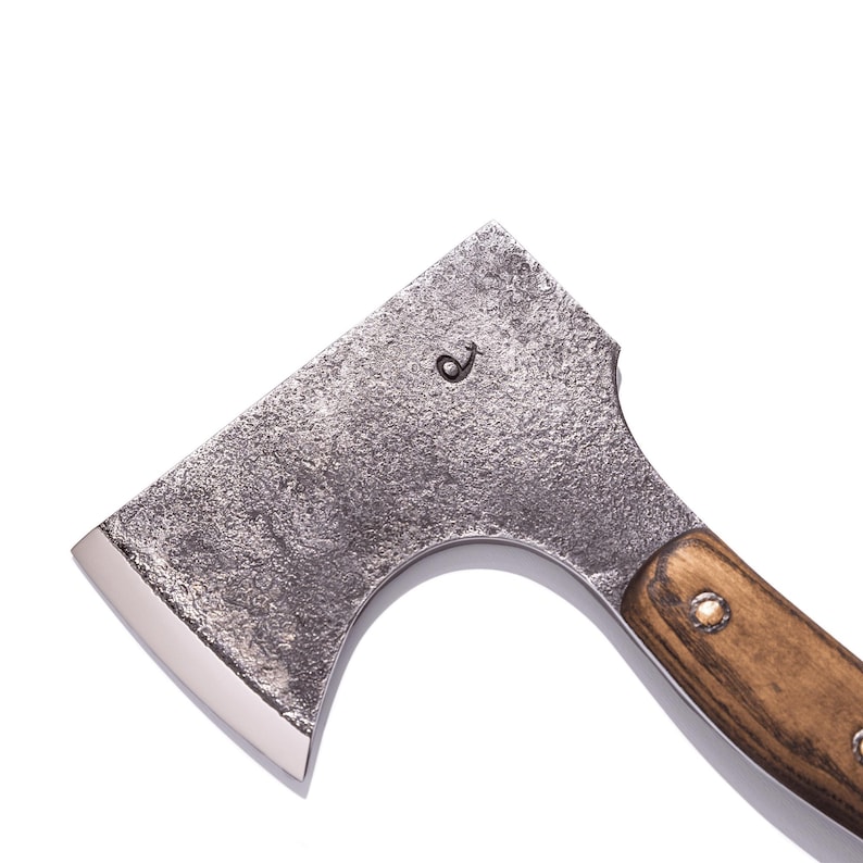 May include: A small, rustic axe with a textured, gray metal head and a polished, silver blade. The wooden handle is a warm brown, secured with metal rivets. The head features a small, etched design.
