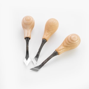 May include: Three wood carving tools with wooden handles and metal blades. The tools are arranged in a fan shape on a white background.
