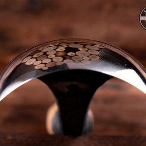 May include: A close-up of a curved, polished metal woodworking tool with a wooden handle. The tool is designed for carving and shaping wood. The metal surface reflects the surrounding environment, showing a pattern of small, round shapes.
