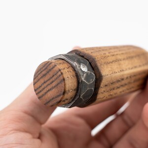 May include: Close-up of a wooden and metal bottle stopper with a hexagonal shape and a metal band around the top.