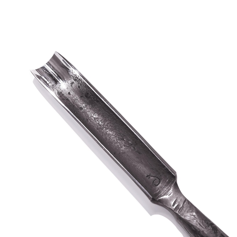 May include: A close-up of a metal woodworking tool with a curved, hollowed-out blade. The tool is designed for carving and shaping wood.