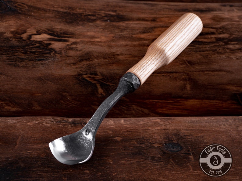 May include: A wooden handled spoon carving tool with a metal scoop. The tool is made by Fadir Tools, Est. 2016.