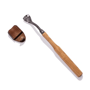 May include: A wooden-handled tool with a metal hook at the end. The tool is lying on a white surface next to a brown leather pouch.