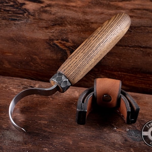 May include: A curved wood carving knife with a brown wooden handle and a leather sheath. The knife is made by Fadir Tools, Est. 2016.
