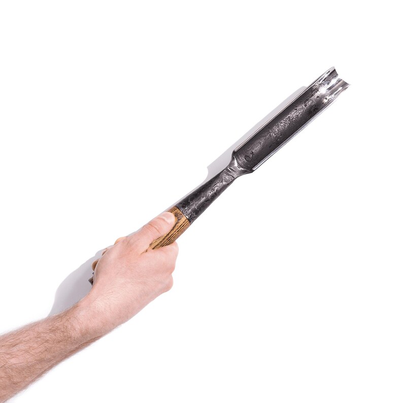 May include: A hand holds a wooden-handled metal chisel with a curved blade.