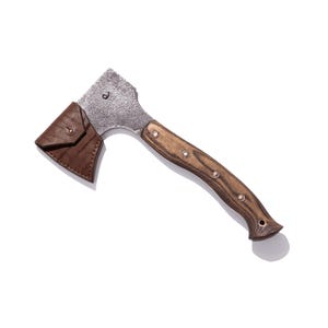 May include: A small, rustic axe with a wooden handle and a metal head. The handle is a dark brown color with silver rivets. A brown leather sheath protects the axe head. The axe is designed for outdoor use.