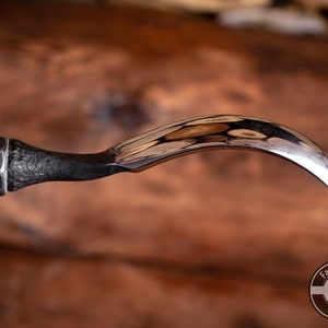 May include: A close-up of a wood carving tool with a curved blade. The tool has a wooden handle and a metal ferrule. The blade is polished and reflects light.