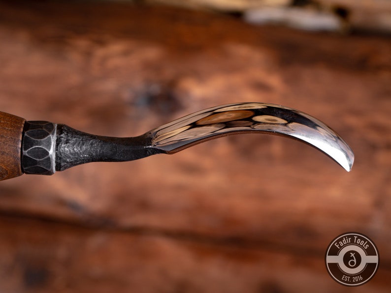 May include: A close-up of a wood carving tool with a curved blade. The tool has a wooden handle and a metal ferrule. The blade is polished and reflects light.