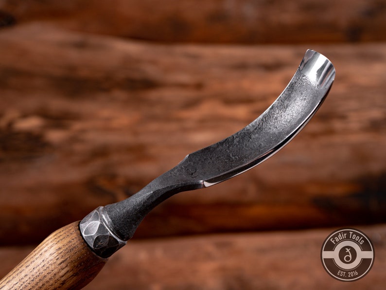 May include: A curved wood carving tool with a wooden handle and a metal blade. The blade is curved and has a sharp edge. The handle is made of wood and has a textured surface. The tool is made by Fadir Tools, Est. 2016.