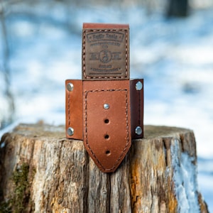 May include: A brown leather tool holder with a brown leather strap and a metal buckle. The holder has a label that reads "Peffir Tools" and "Handcrafted, Made in America Products".