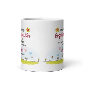 May include: White ceramic mug with a colorful design and text that reads "Eine gro&szlig;artige Ergoterapeutin ist schwer zu finden, aber unm&ouml;glich zu vergessen!" on one side and "Eine gro&szlig;artige Ergoterapeutin ist schwer zu finden, aber unm&ouml;glich zu vergessen!" on the other side.