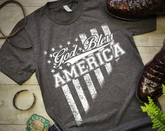 Puede incluir: Una camiseta gris oscura con un diseño de bandera estadounidense blanca desgastada y el texto "God Bless America".
