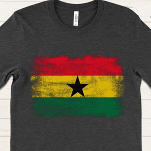 May include: A dark grey t-shirt with a distressed, faded print of the flag of Ghana. The flag is red, yellow, green, and black with a black star in the center.