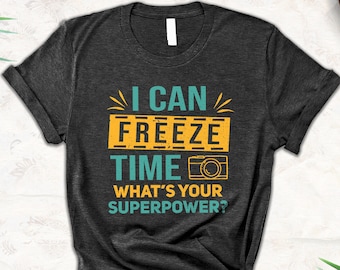 May include: Dark grey t-shirt with a yellow and blue graphic that says "I can freeze time. What's your superpower?" with a camera icon.