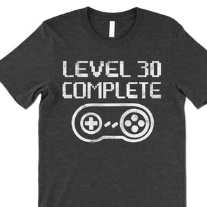May include: A dark gray t-shirt with a white graphic that says "Level 30 Complete" with a pixelated video game controller underneath.