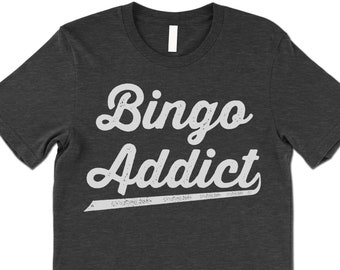 May include: A dark grey t-shirt with the text "Bingo Addict" in white, stylised lettering. The text has a vintage, distressed look.