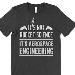 Op de afbeelding: Donkergrijs T-shirt met witte tekst die luidt "Het is geen raketwetenschap, het is lucht- en ruimtevaarttechniek." Een klein raketje bevindt zich boven de tekst.