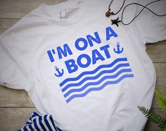 Może przedstawiać: Biała koszulka z niebieskim tekstem, który mówi "I'm on a boat" z niebieską kotwicą i falistymi liniami.