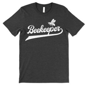 Puede incluir: Una camiseta gris oscuro jaspeada con un gr&aacute;fico blanco de estilo vintage de una abeja y la palabra "Beekeeper".