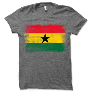 May include: A gray t-shirt with a distressed, faded design of the flag of Ghana. The flag features red, yellow, and green stripes with a black star in the center.