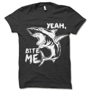 May include: A dark grey t-shirt with a white graphic of a shark with its mouth open and the text "Yeah, Bite Me".