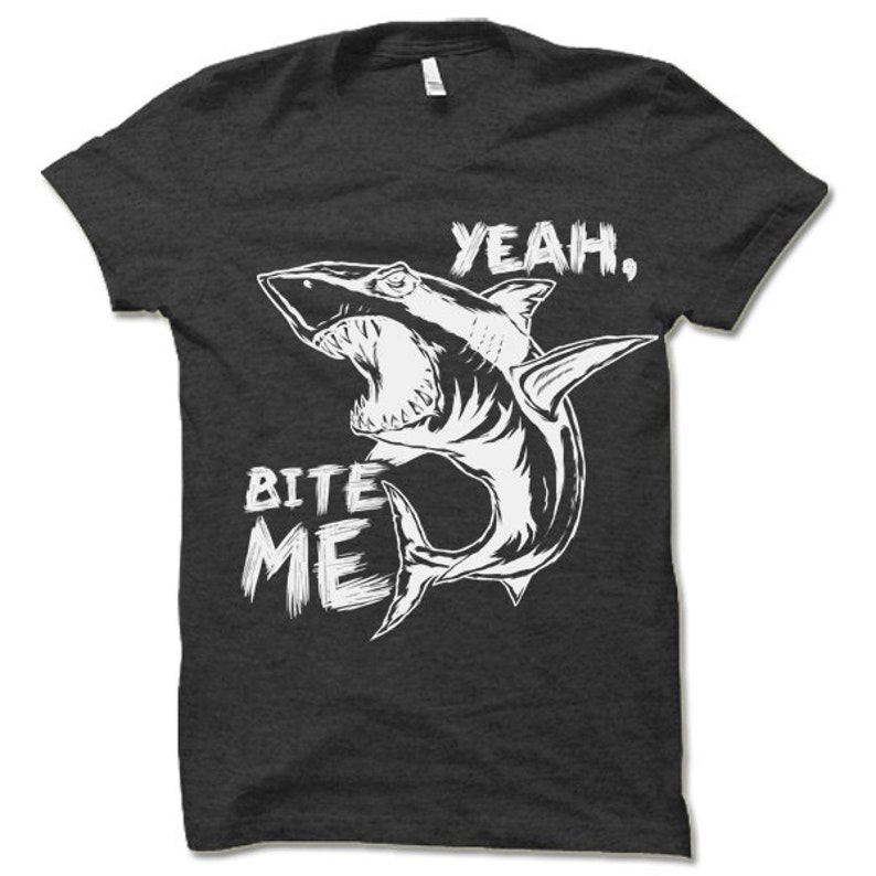 May include: A dark grey t-shirt with a white graphic of a shark with its mouth open and the text "Yeah, Bite Me".